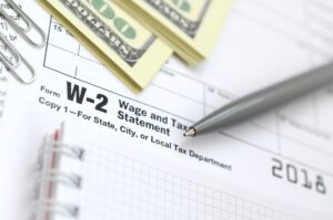 The pen, notebook and dollar bills is lies on the tax form W-2 W